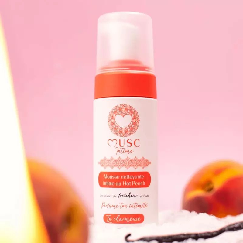 Mousse Nettoyante Intime Hot Peach sur comptoir marbre avec serviette et pêches fraîches, évoquant l