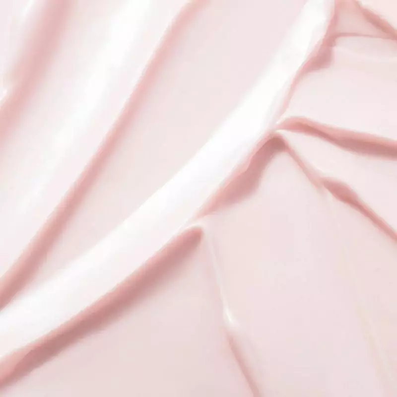 Texture crémeuse rose du Baume-Huile Prodigieuse Hyalu Boost NUXE étalée sur tissu rose doux, révéla