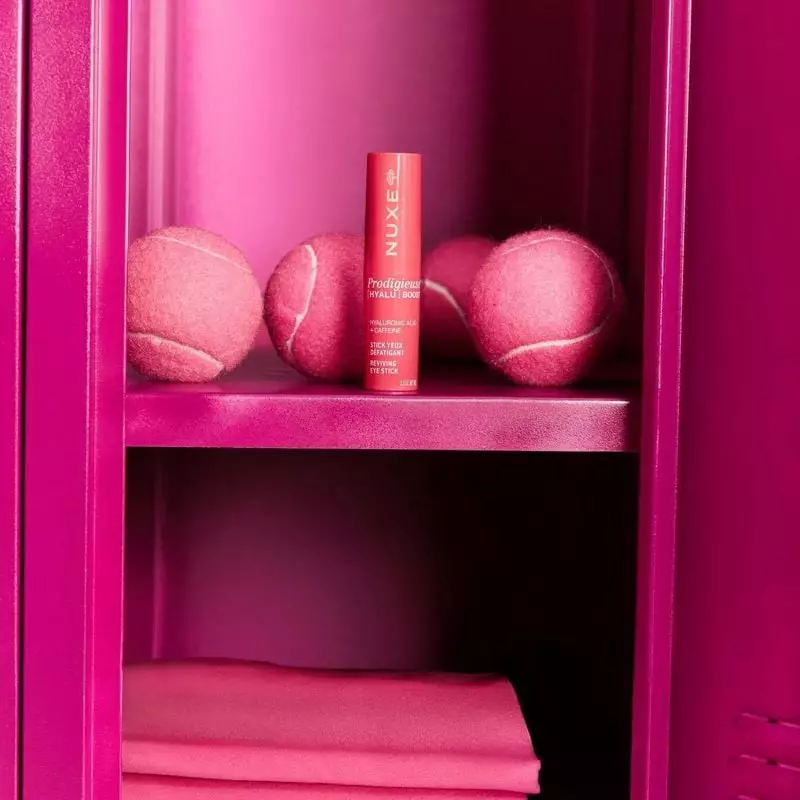 Stick yeux NUXE 685914 rose présenté dans un casier rose ouvert avec balles de tennis roses et tissu