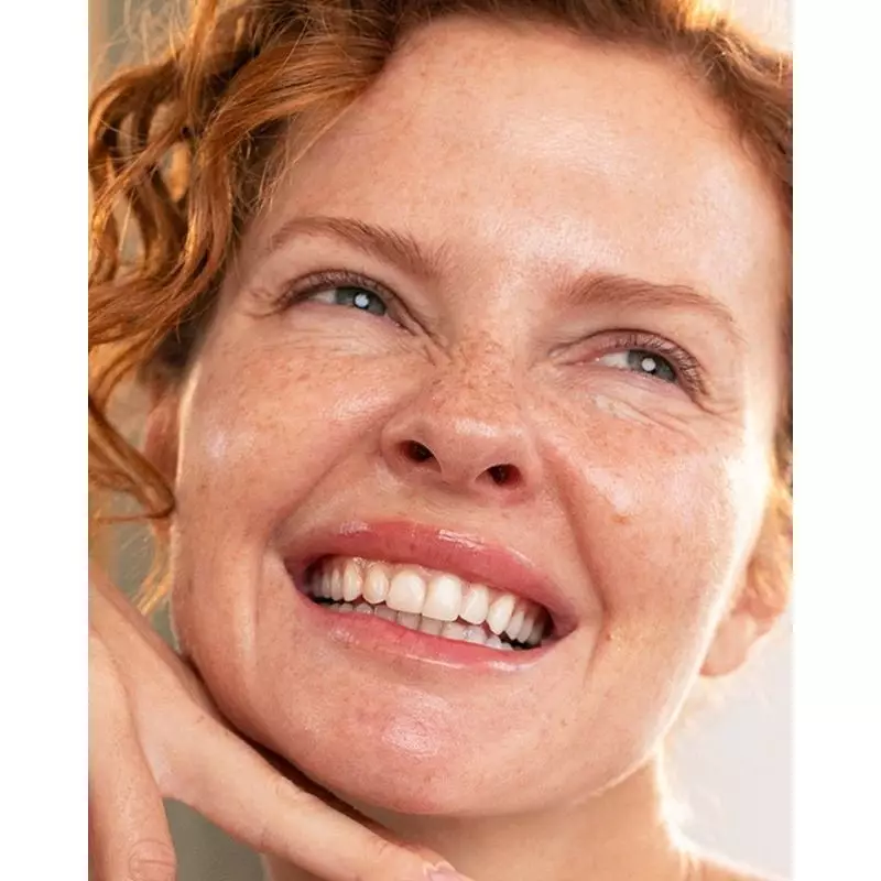 Femme souriante aux taches de rousseur et cheveux roux bouclés tenant le flacon SVR Densitium B Séru