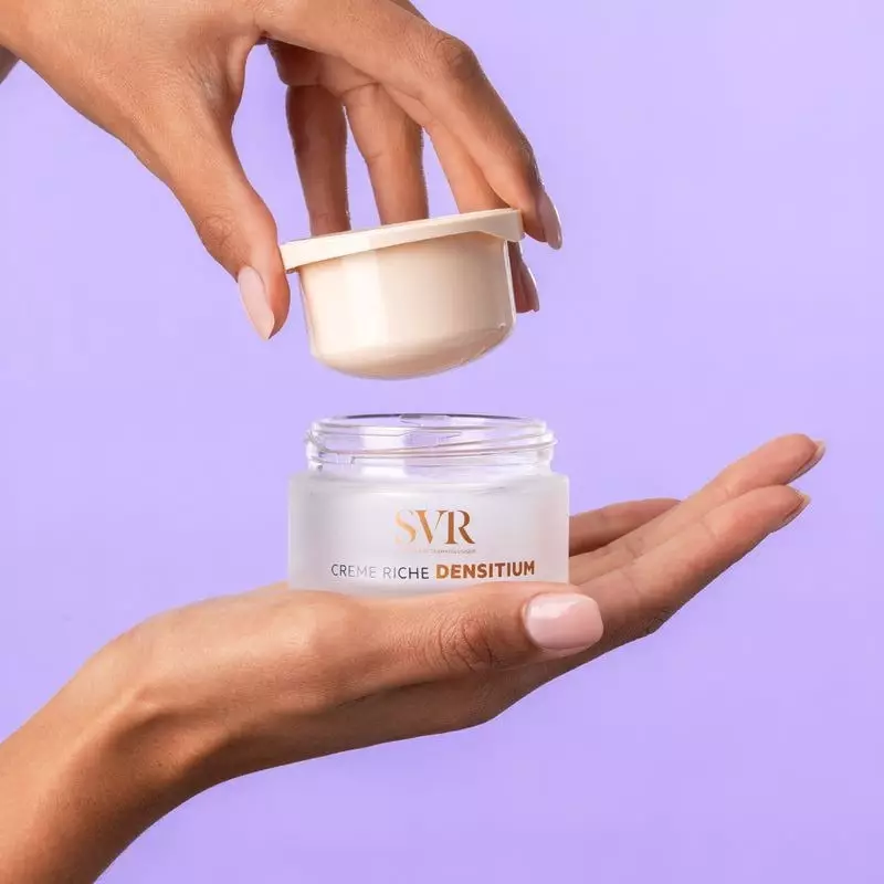 Main tenant le pot SVR Densitium Crème Riche ouvert avec godet amovible, révélant la texture crémeus