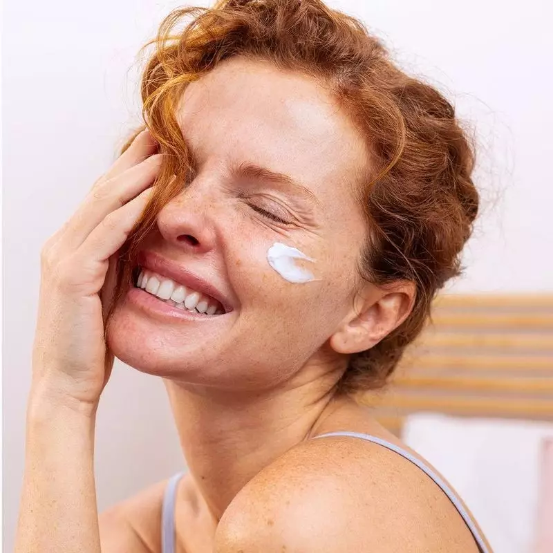 Femme souriante aux cheveux roux appliquant la Crème Riche SVR DENSITIUM sur son visage, application
