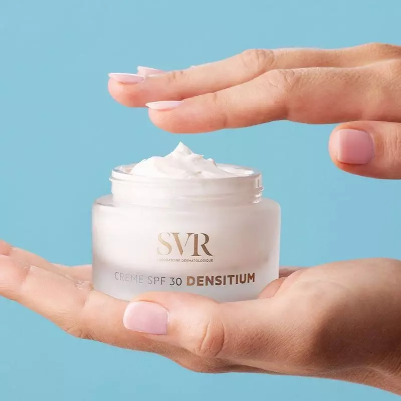 Mains de femme tenant le pot ouvert de SVR Densitium Crème SPF30, révélant une généreuse crème blanc