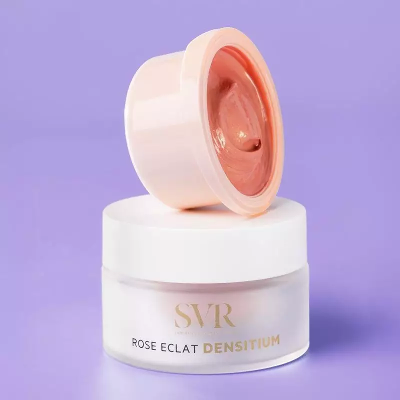 Gros plan du pot SVR DENSITIUM Rose Éclat ouvert avec crème rose scintillante sur fond violet, à côt