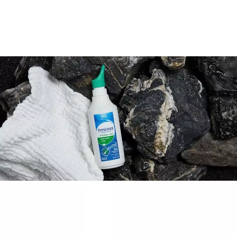 Flacon de spray nasal Physiomer Spray Doux posé sur roches noires avec tissu blanc, corps blanc, éti
