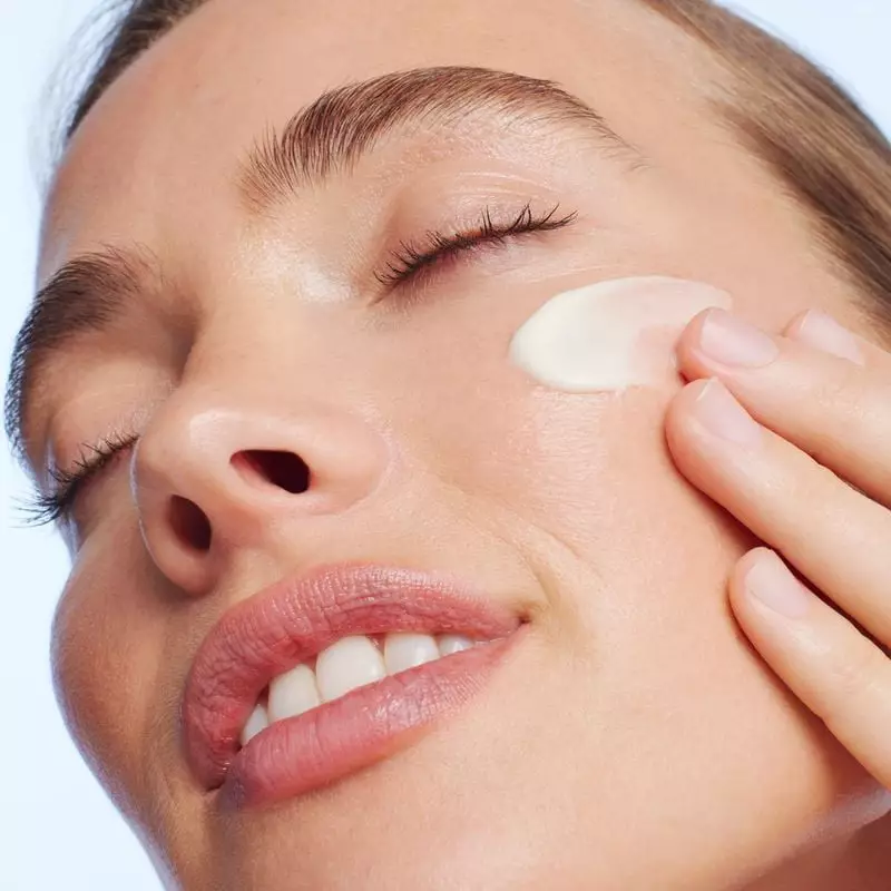 Gros plan d'une femme appliquant la crème blanche onctueuse NUXE Merveillance Lift sur son visage, t