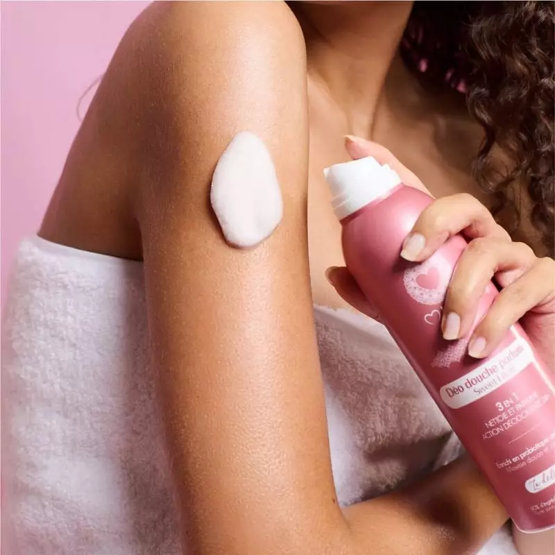 Femme en serviette appliquant une mousse crémeuse blanche du déo-douche Musc Intime Sweet Litchi sur