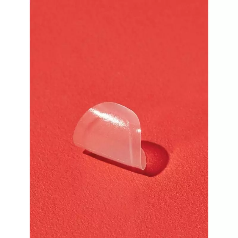 Gros plan d'un patch hydrocolloïde COSRX AC Collection ovale large translucide sur fond rouge, textu