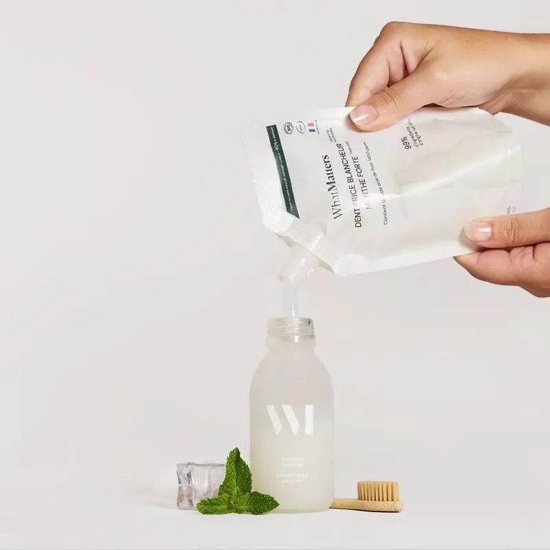 Main versant la recharge éco dans une bouteille en verre transparent avec feuilles de menthe, glace 