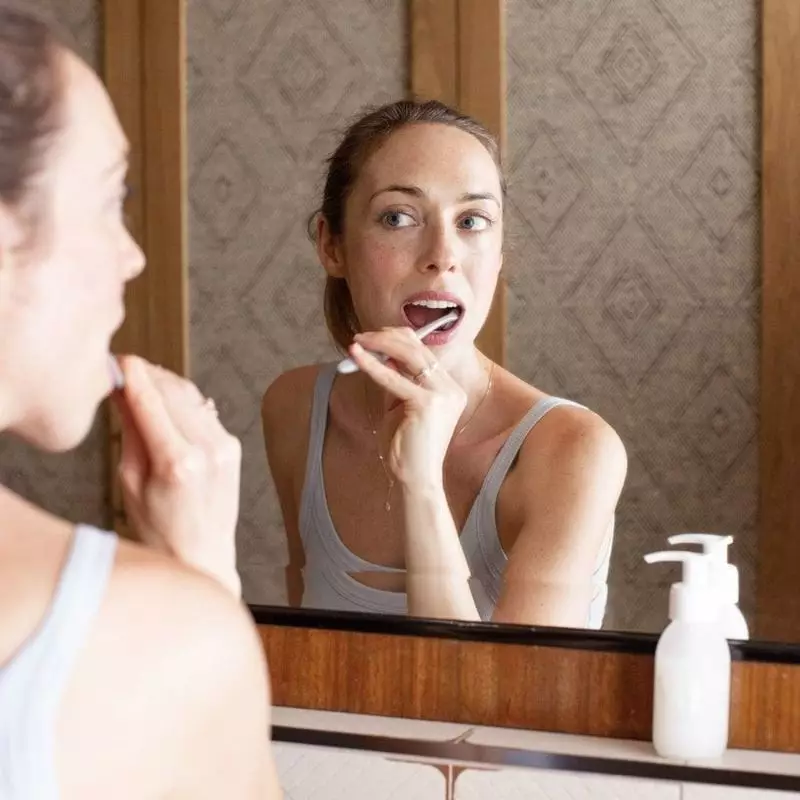 Femme se brossant les dents dans le reflet du miroir avec distributeur blanc What Matters à proximit