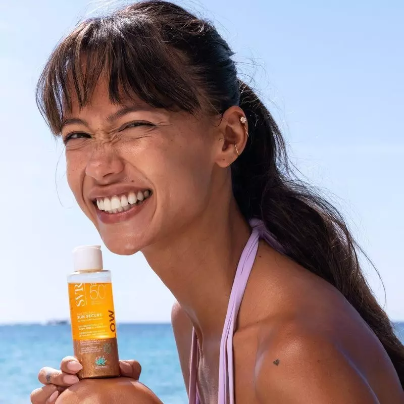 Gros plan sur femme joyeuse faisant un clin d'œil, tenant le flacon SVR Eau Solaire SPF50+ près de s