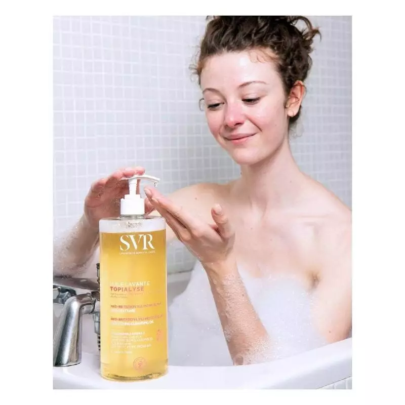 Femme souriante dans baignoire tenant flacon SVR Topialyse, appliquant mousse du distributeur avec b