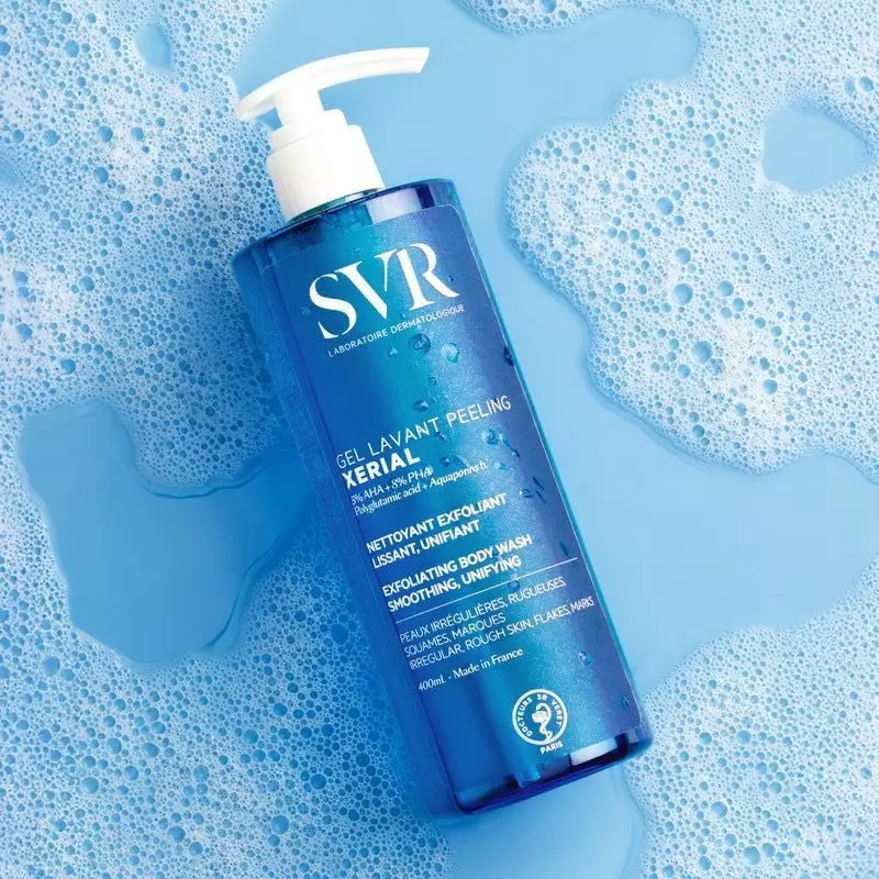Gros plan sur le flacon SVR Xérial Gel Lavant Peeling dans un décor d'eau mousseuse.