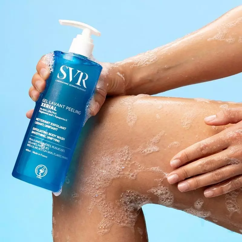 Personne appliquant le Gel Lavant Peeling SVR Xérial sur sa jambe, créant une mousse onctueuse.