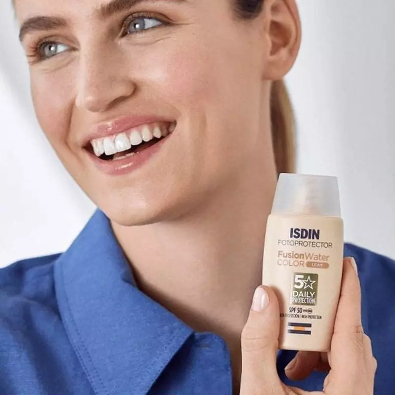 Femme souriante tenant le tube ISDIN Fusion Water Color Light SPF 50 près de son visage, démontrant 