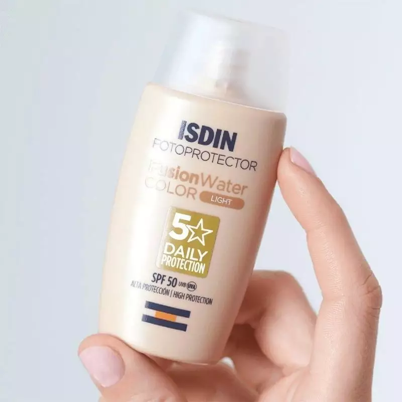 Main tenant le tube ISDIN Fusion Water Color Light SPF 50 incliné, affichant les étiquettes clés com