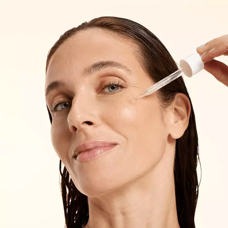 Mains appliquant le sérum Embryolisse au pipette, goutte claire tombant de la bouteille en vue gros 