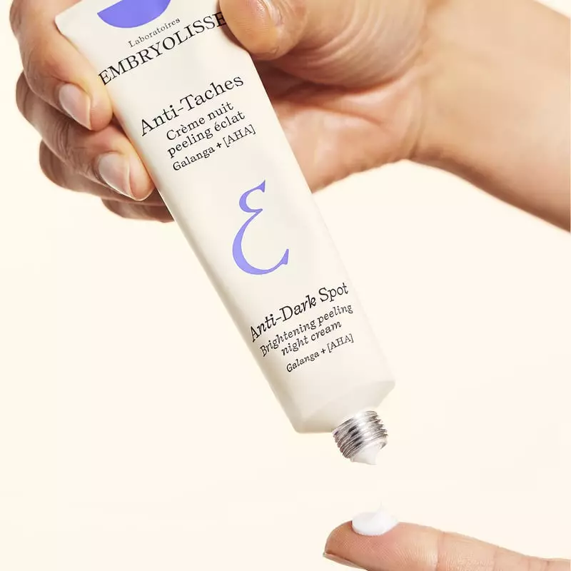 Main pressant le tube Embryolisse 1065085, dispensant crème blanche sur le doigt, vue gros plan appl