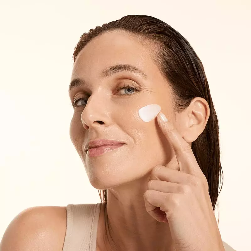 Femme appliquant la crème de nuit Embryolisse 1065085 sur sa joue, souriante, peau rayonnante, en dé