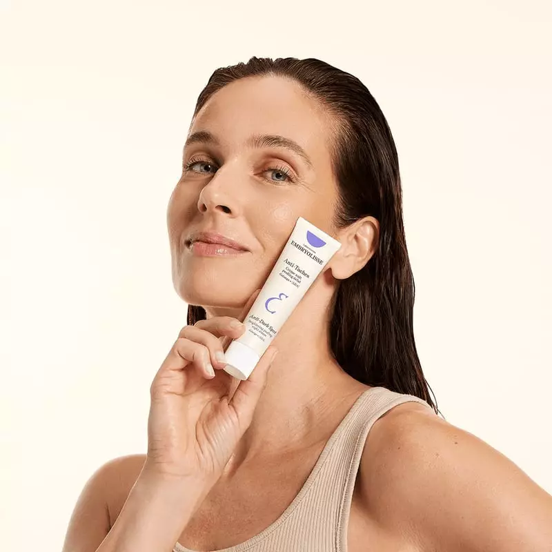 Modèle tenant le tube Embryolisse 1065085 près de son visage, appliquant la crème sous les yeux, pea