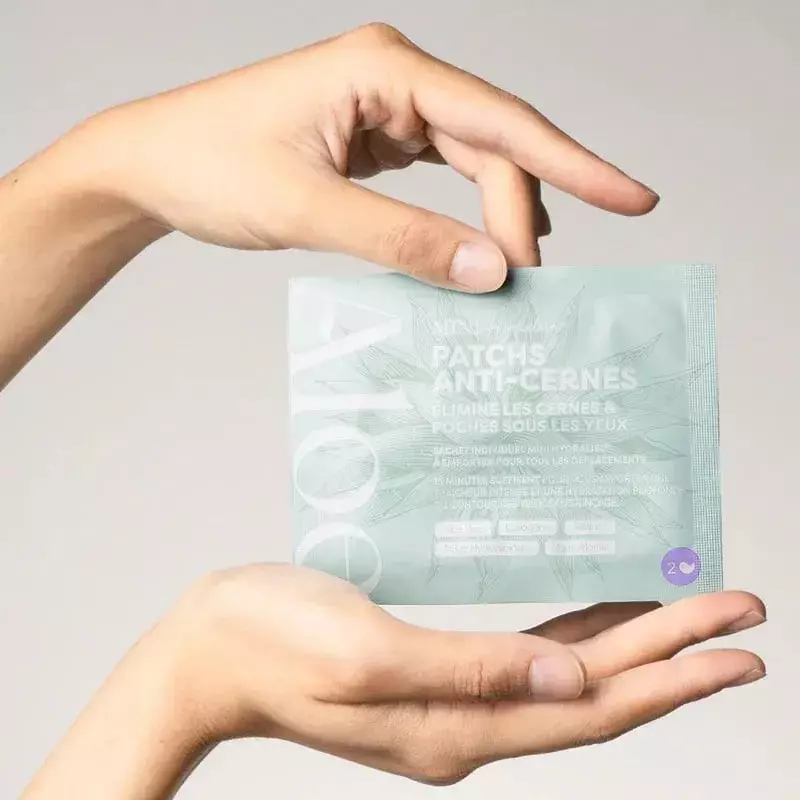 Femme souriante yeux fermés appliquant deux patchs hydrogel verts Aloe Paris sous les yeux, main tou