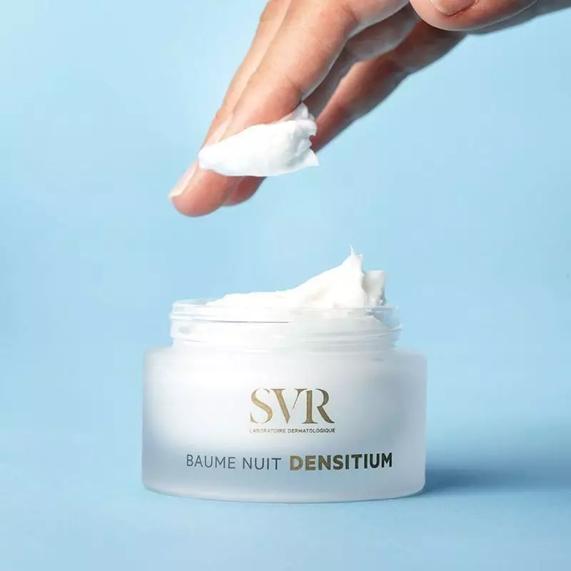 Une main prélève une noisette de crème riche du pot SVR Densitium Baume Nuit Recharge.