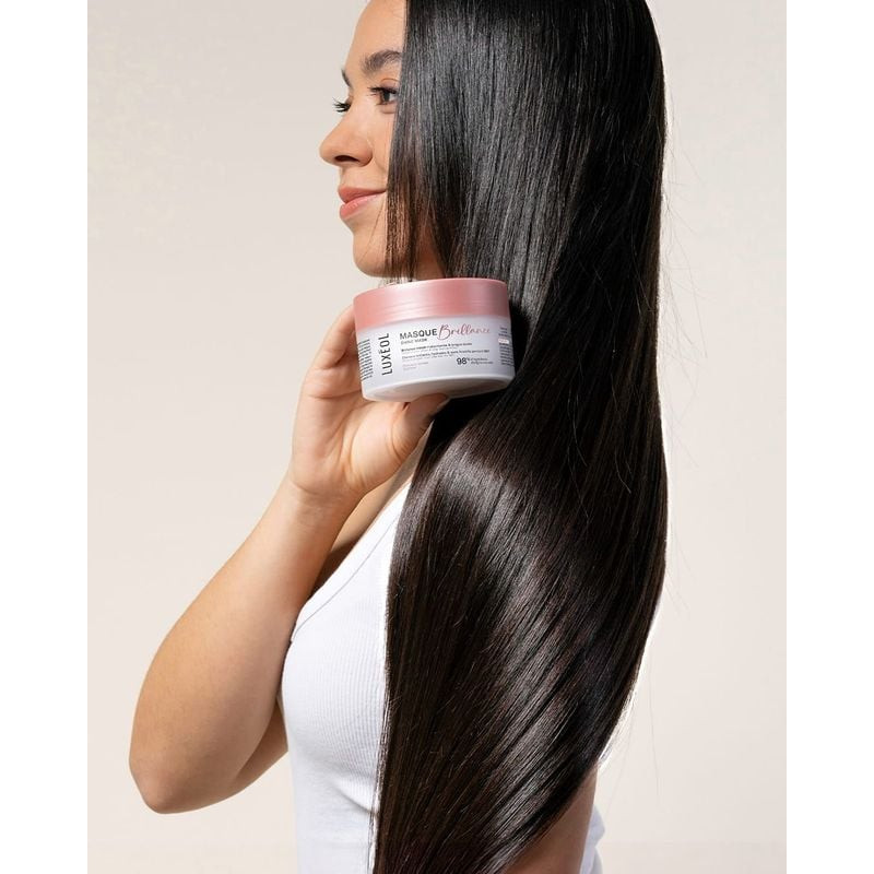 Modèle aux cheveux lisses noirs brillants tenant le pot Masque Brillance Luxéol, soulignant des résu