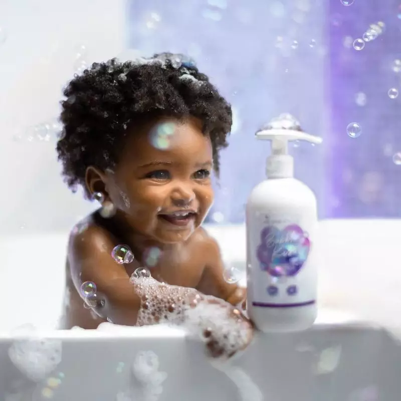 Bébé heureux aux cheveux texturés profitant du bain, tenant le flacon Bubble Kiss Les Secrets de Lol