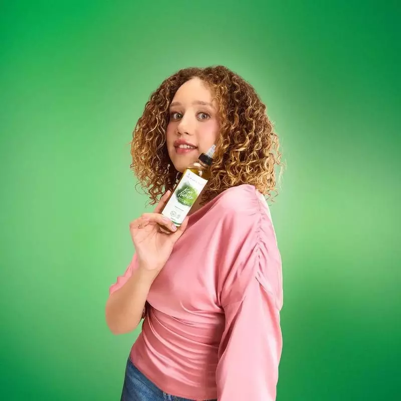 Femme souriante aux cheveux bouclés tenant le flacon d'huile capillaire Les Secrets de Loly Kurl Nut