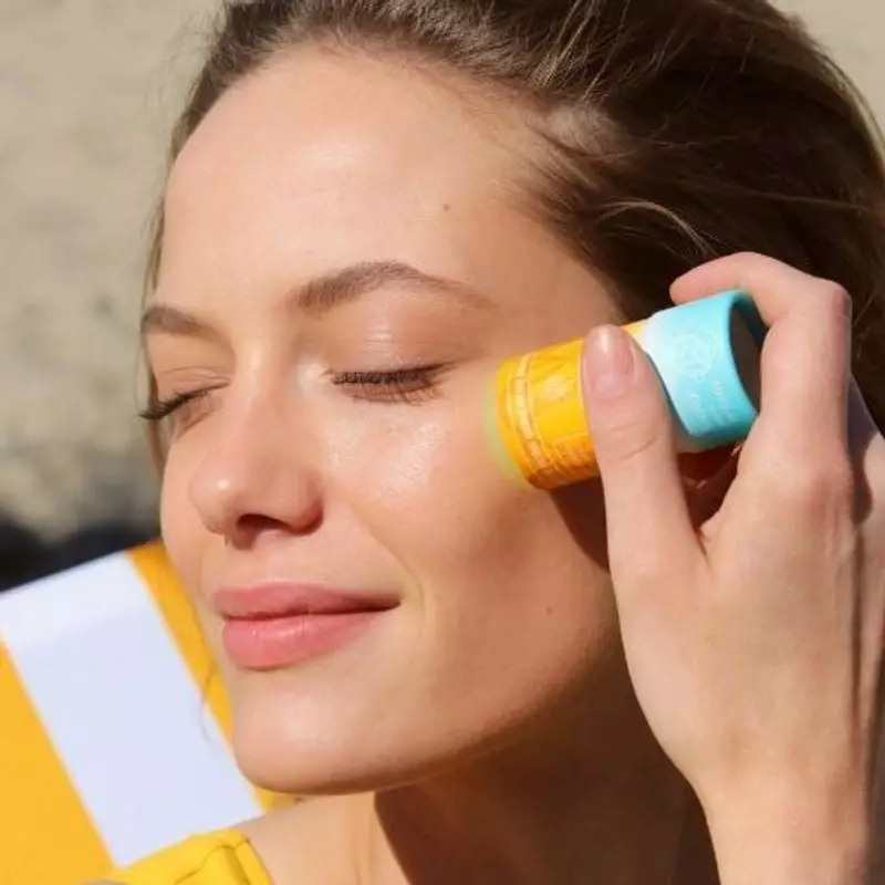 Femme appliquant le stick solaire anti-âge Respectueuse SPF50+ sur son visage en plage ensoleillée, 