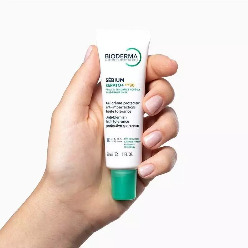 Main de femme tenant le tube Bioderma Sébium Kerato+ SPF30 30ml, format pratique et branding pour so