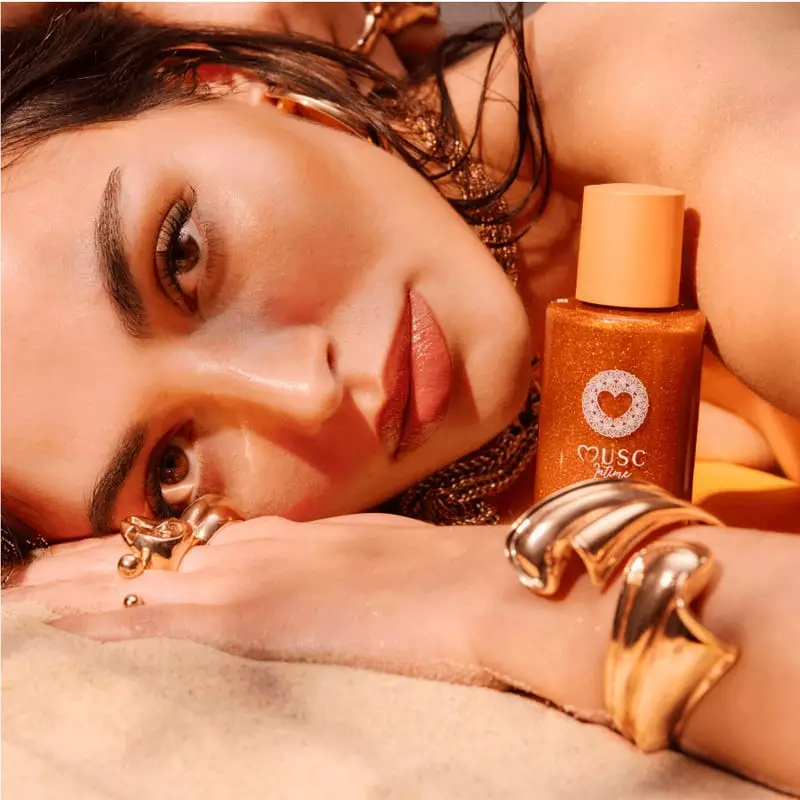 Photo lifestyle d'une femme appliquant l'Huile Glow Pailletée Amber Flower sur son bras, révélant un