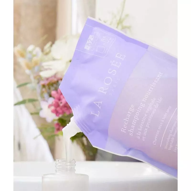 Recharge de shampoing nourrissant La Rosée posée sur un comptoir de salle de bain avec des plantes v