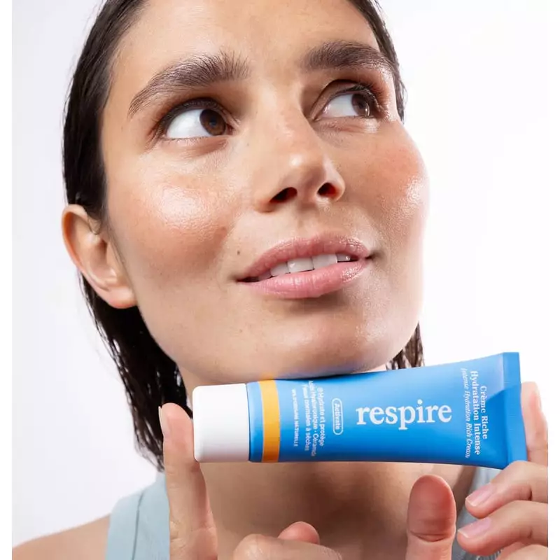 Femme appliquant Respire La Crème Riche Hydratation Intense sur son visage dans une salle de bain lu