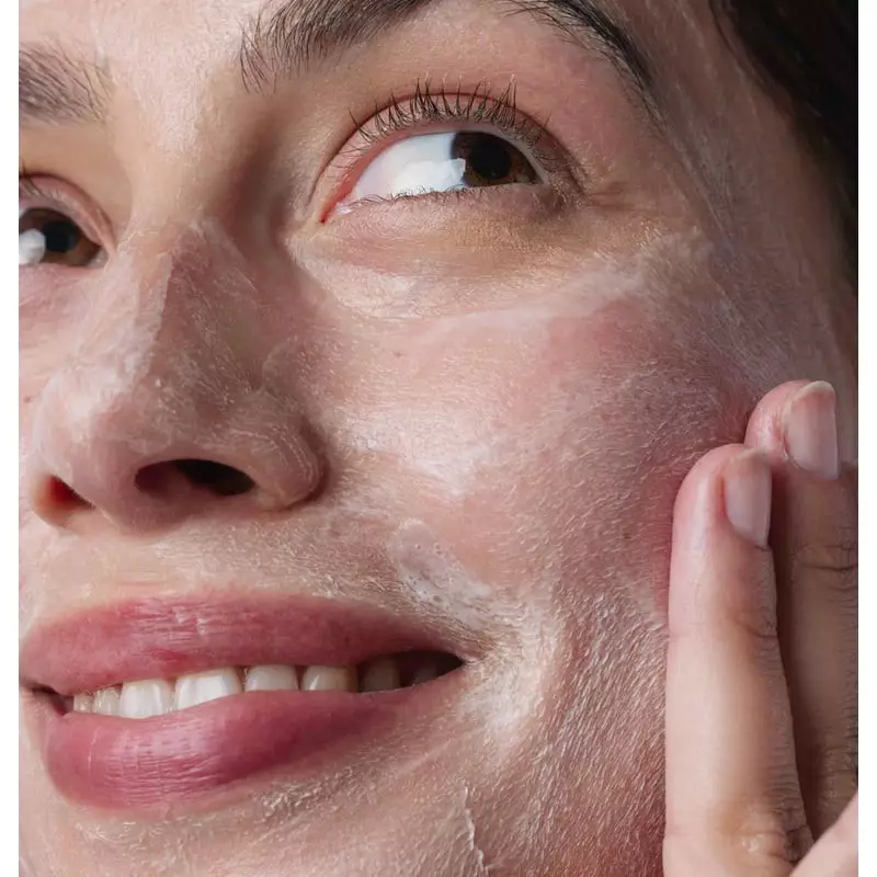 Femme appliquant le Soin Nettoyant Visage Stick Respire sur son visage dans une salle de bain lumine