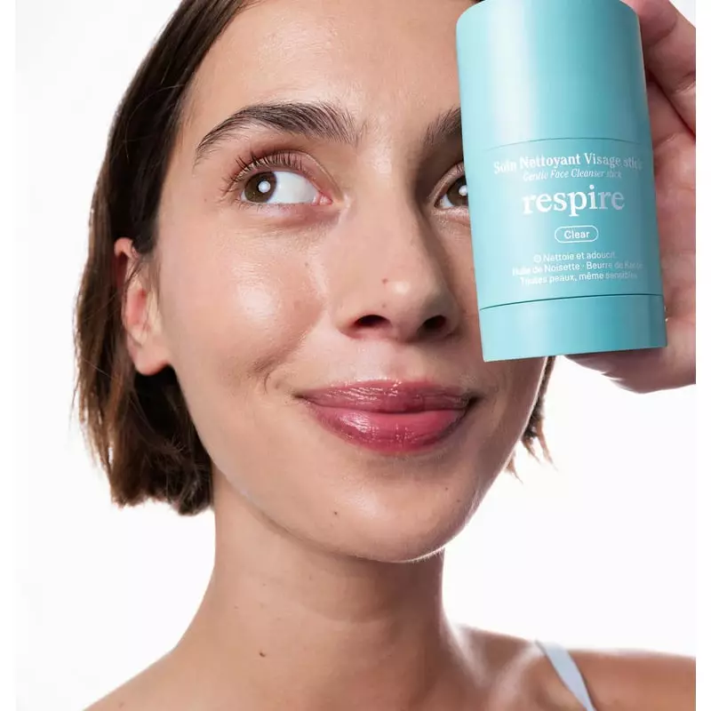 Femme à la peau nette et lumineuse après utilisation du Soin Nettoyant Visage Stick Respire, tenant 