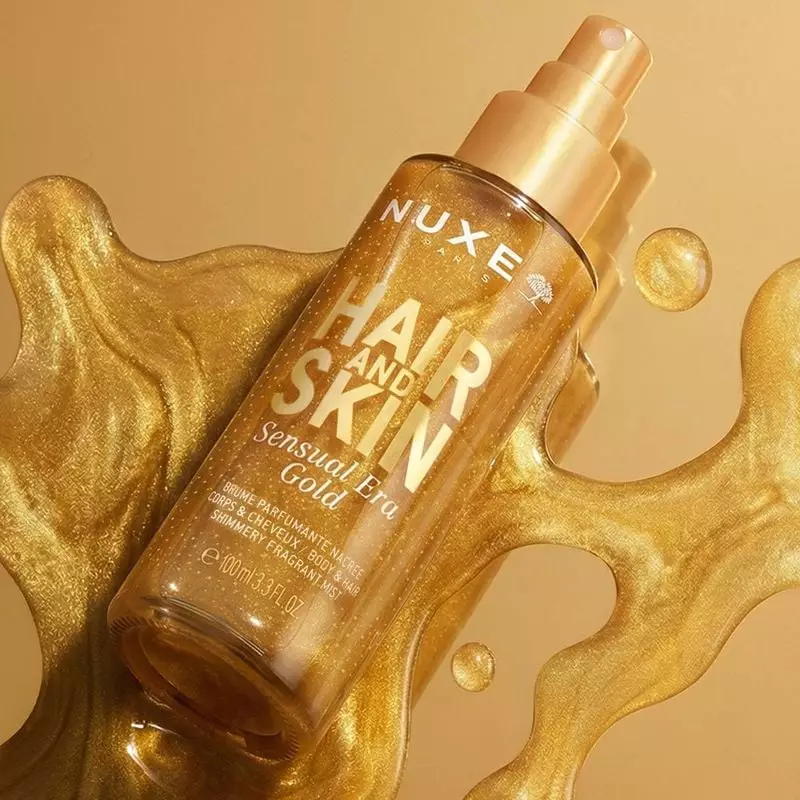Femme vaporisant la brume corps et cheveux NUXE Sensual Era Gold, créant une aura scintillante.