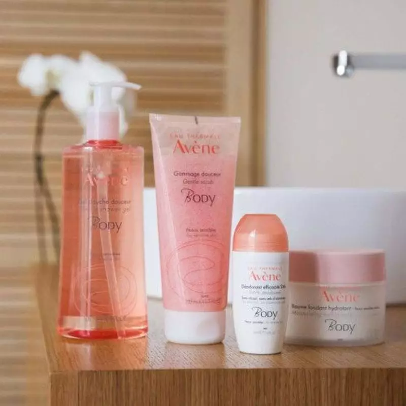 Femme appliquant le déodorant Avène 24h sous son bras, souriant dans une salle de bain lumineuse.