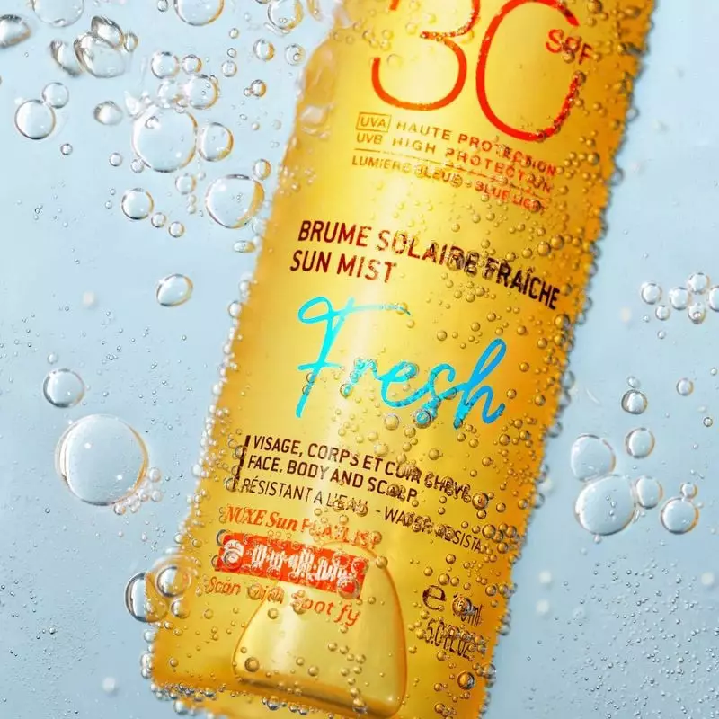 Nuxe Brume solaire fraîche SPF30 150ml posée sur du sable avec accessoires estivaux