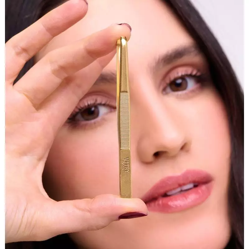 Femme utilisant une pince à épiler dorée Vitry 2067656 pour dessiner ses sourcils dans un espace bea