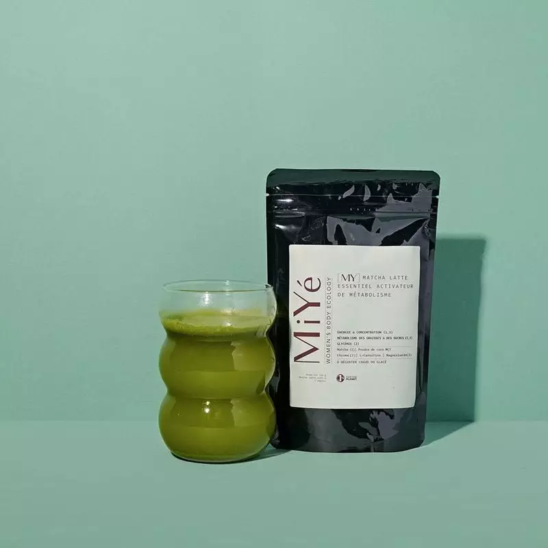 Photo d'ambiance du pot MiYé Matcha Latte à côté d'une tasse en céramique de matcha latte vert fuman