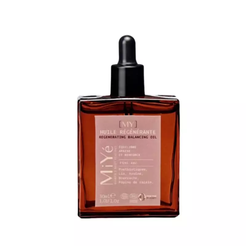 Bouteille d'huile régénérante MiYé en flat lay avec graines de jojoba, avoine et feuilles vertes