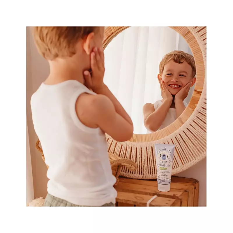 Enfant souriant à son reflet dans le miroir, tube de crème hydratante bio 100 ml Baby Green posé sur