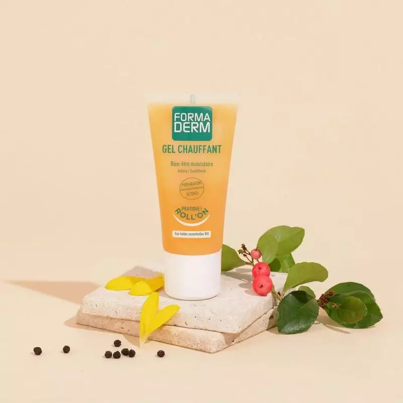 Tube Formaderm Gel Chauffant stylisé sur pierre avec feuilles, baies et grains de poivre sur fond be