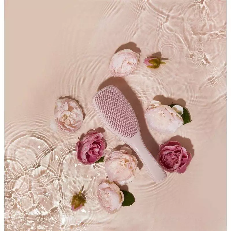 Brosse Tangle Teezer Rose Millennial flottant sur une eau ondulée, entourée de fleurs roses