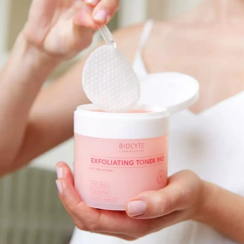 Mains soulevant un coussinet tonique exfoliant Biocyte texturé du pot rose, montrant le côté gaufré 