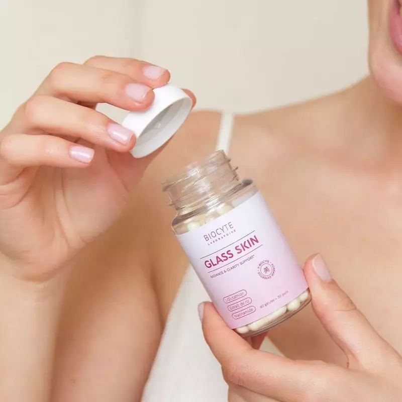Femme tenant le pot Biocyte Glass Skin, dévissant le couvercle blanc dans une scène lumineuse