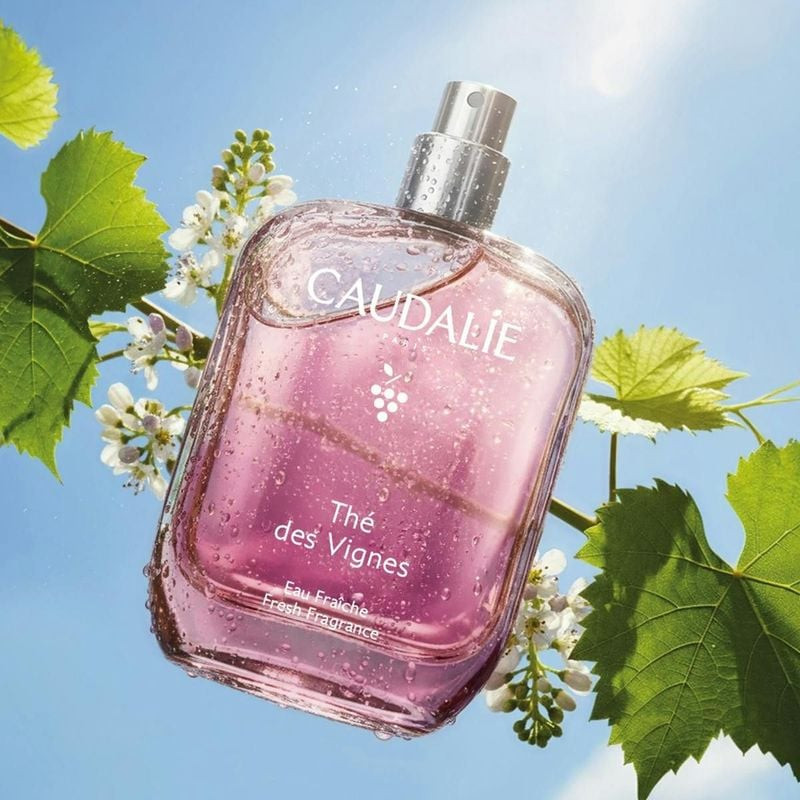 Flacon Caudalie Thé des Vignes 50 ml avec gouttes d'eau parmi des feuilles de vigne et fleurs blanch
