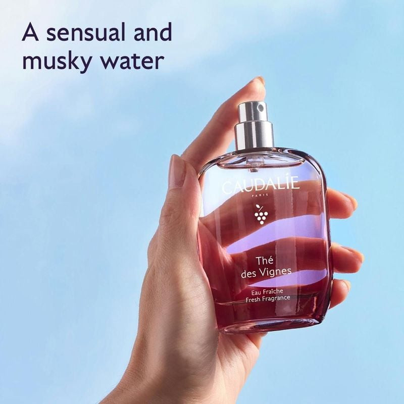Main tenant le flacon d'eau fraîche Caudalie Thé des Vignes 50 ml sur fond de ciel bleu, eau musquée
