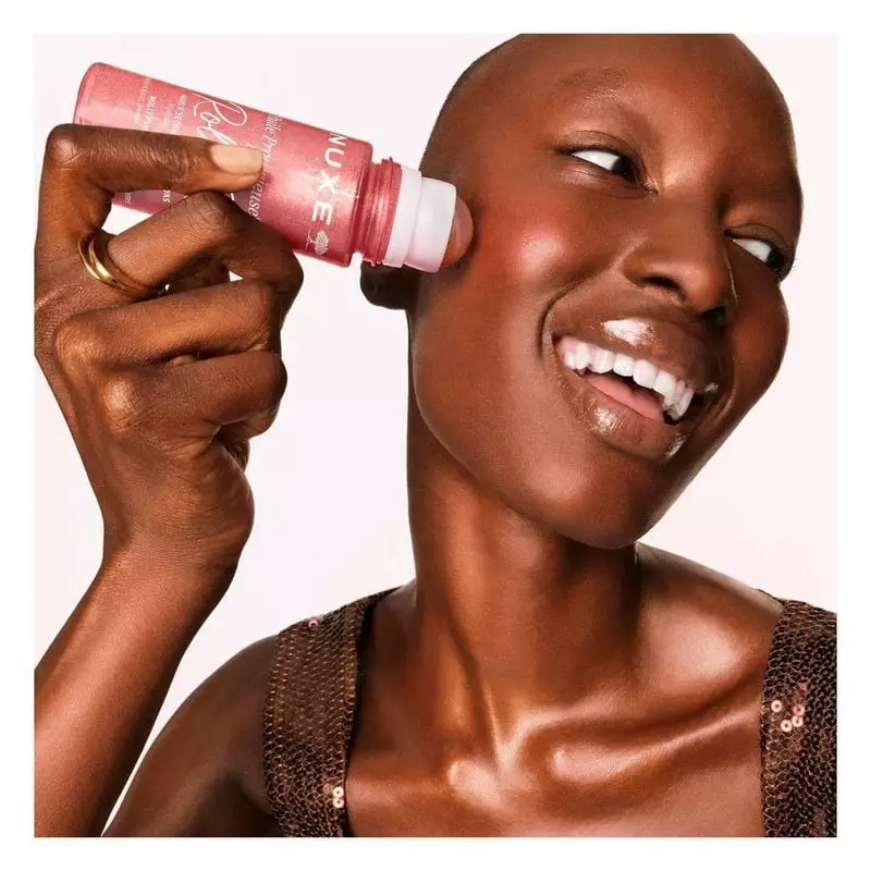 Mannequin au teint lumineux appliquant le roll-on Nuxe Huile Prodigieuse Or Florale sur sa joue